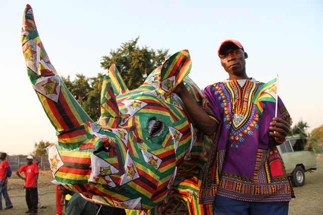 Paricipants of the Victoria Falls street Carnival stand next to a Rhino dressed in Zimbabwean colours