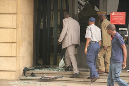 Police officers assess the damage on the glass door and windows at Allied Bank in Harare yesterday                                                        morning